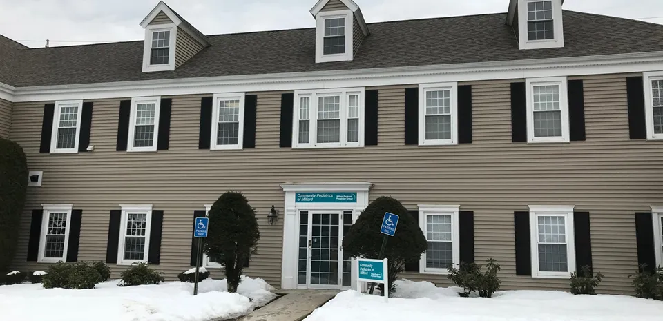 The outside of Community Pediatrics of Milford. There is snow on the ground and the grey building has the practice sign out front.