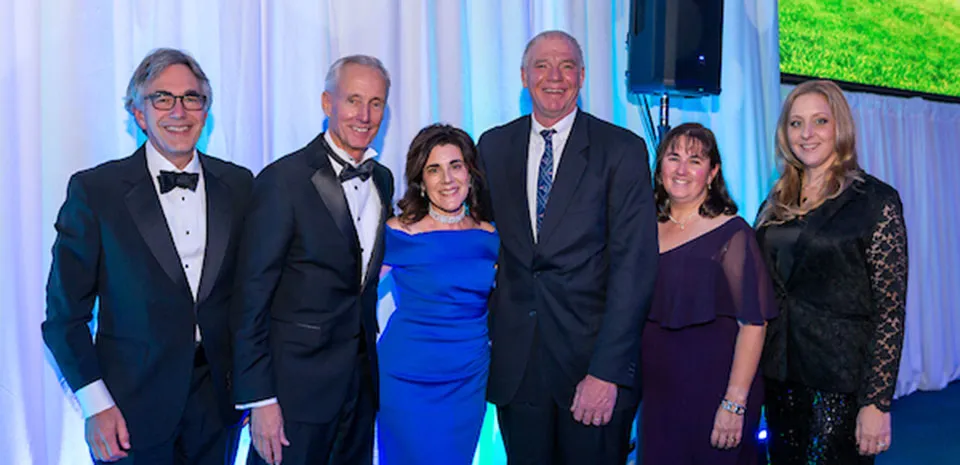 A group of six people in formal attire poses for a picture, smiling.