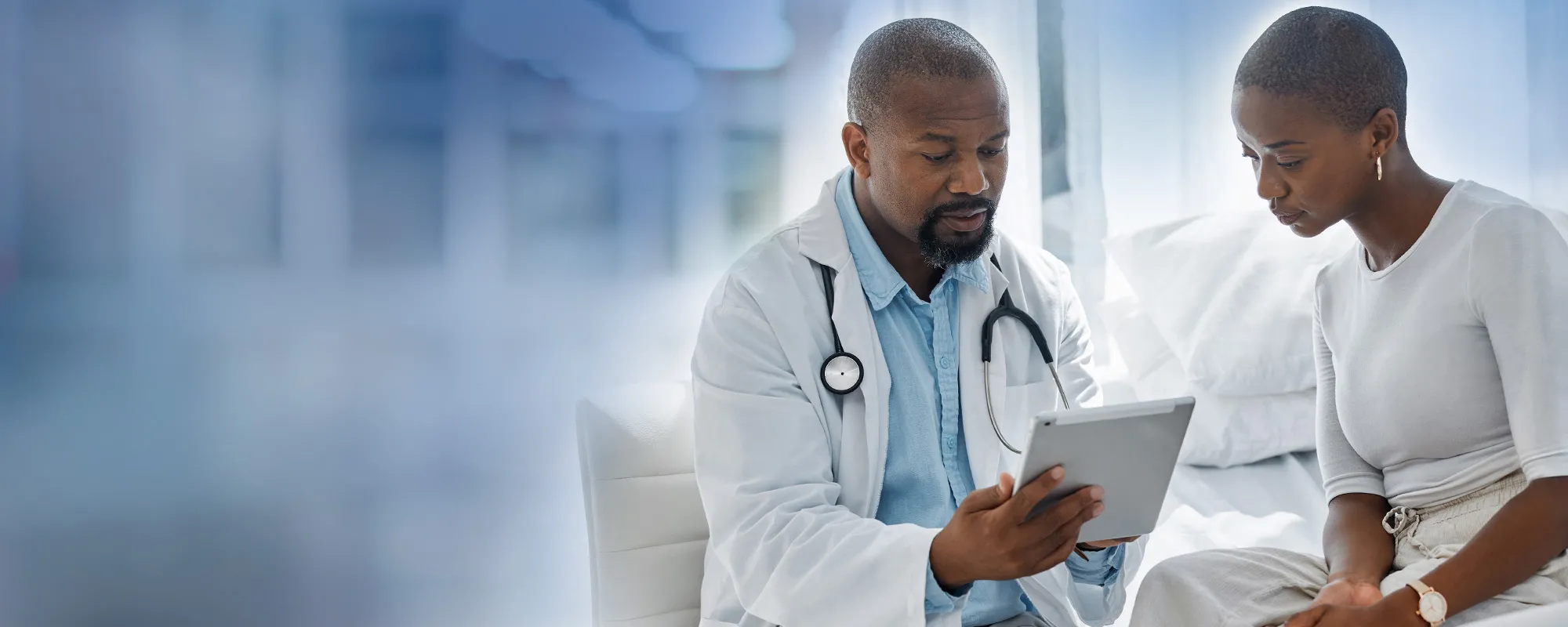 A doctor meets with a patient, sharing something on a tablet screen.