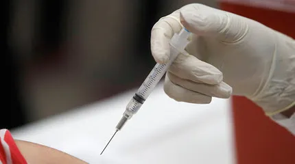The gloved hand of a health care worker holds a shot just above the skin of a recipient.