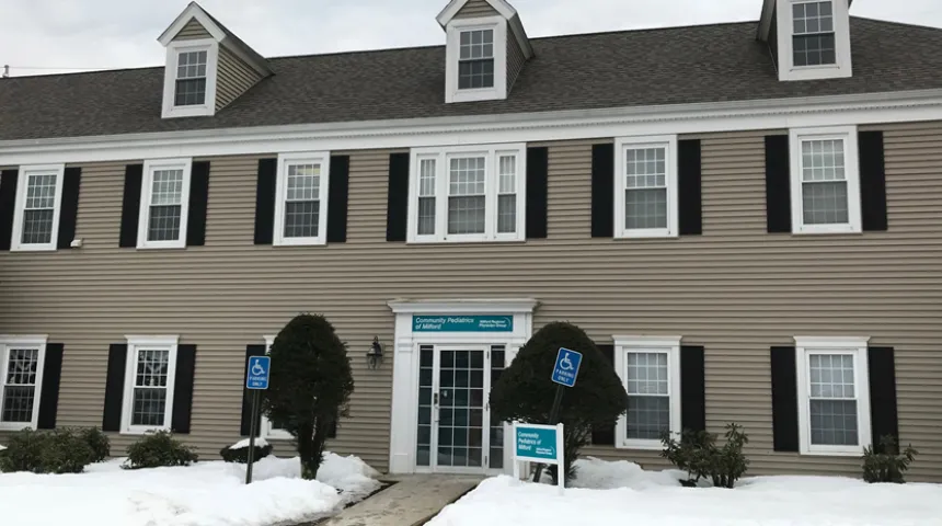 The outside of Community Pediatrics of Milford. There is snow on the ground and the grey building has the practice sign out front.