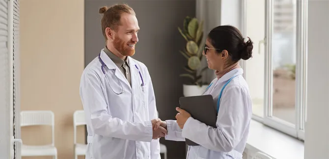 Two doctors in white coats facing each other and shaking hands.