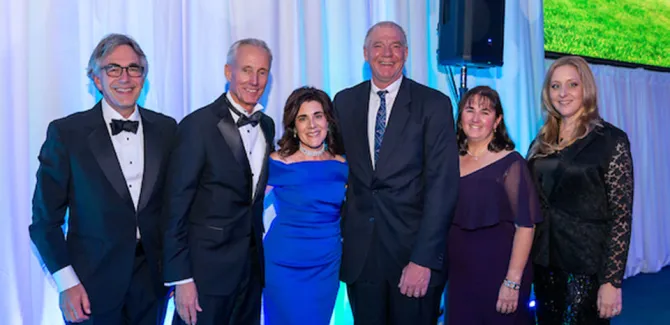 A group of six people in formal attire poses for a picture, smiling.