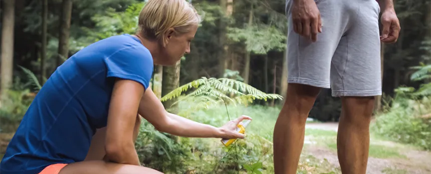 couple putting on bug spray while walking in the woods